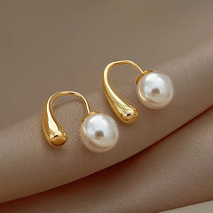 Gold-tone arc hoop earrings with white pearls, angled close-up