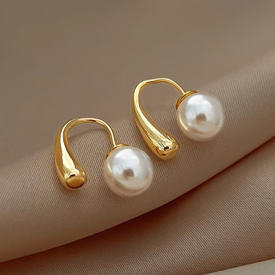 Gold-tone arc hoop earrings with white pearls, angled close-up