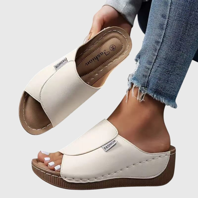 White wedge sandals with wide strap and open toe, stitched trim and textured sole