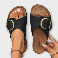 Black sandals with oval gold buckle and tan footbed, open-toe slide