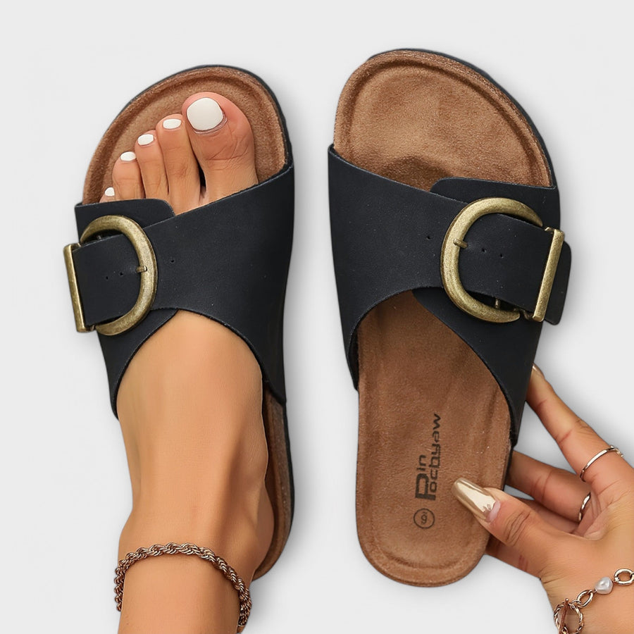 Black sandals with oval gold buckle and tan footbed, open-toe slide