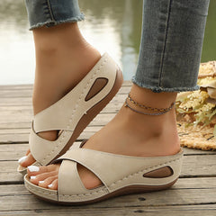 Beige open-toe slide sandals with cross straps, stitched sole, and ankle chain strap