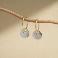 Gold hoop earrings with hanging brushed silver disc charms on display bar