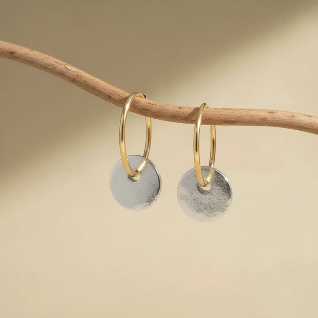 Gold hoop earrings with hanging brushed silver disc charms on display bar