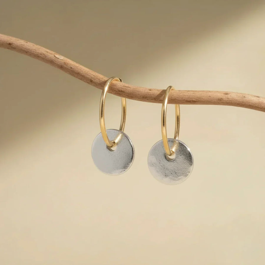 Gold hoop earrings with hanging brushed silver disc charms on display bar