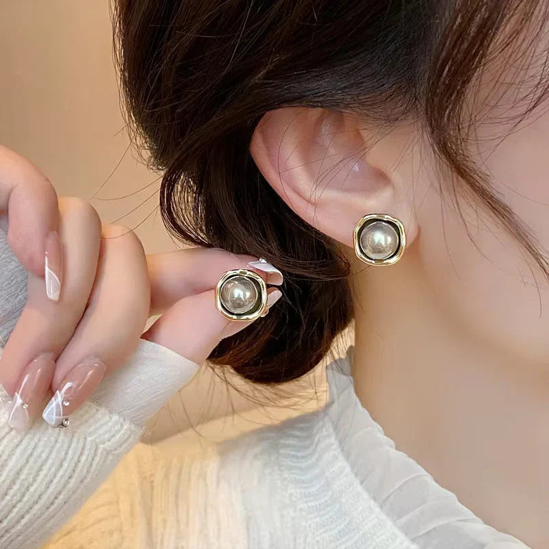 Round gold-tone pearl stud earrings on a model's ear