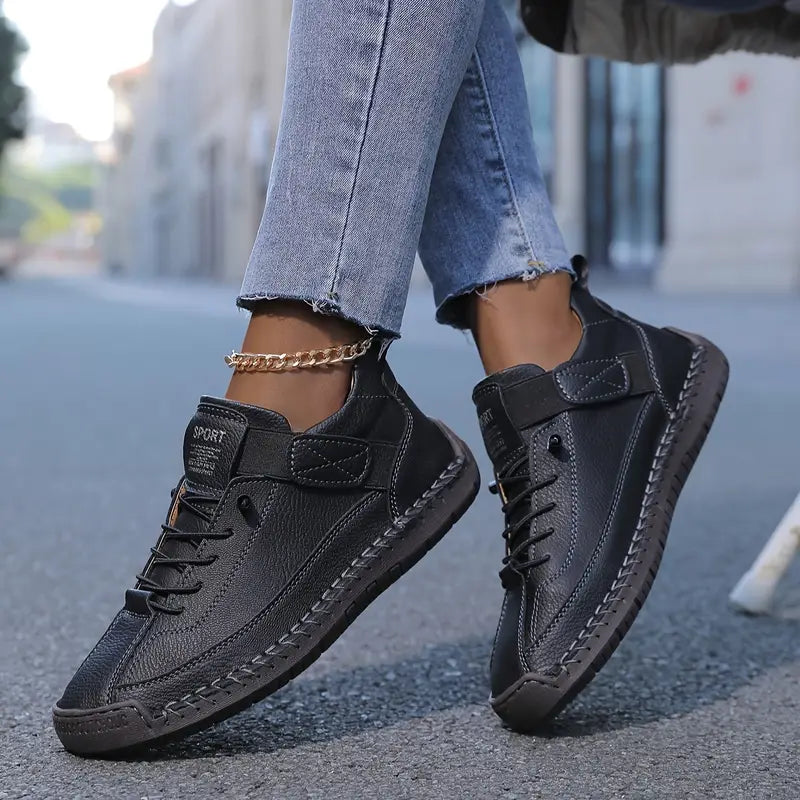 Black comfort sneakers with lace-up front, textured sole, and chain ankle strap