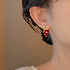 Wine red heart hoop earrings with gold-tone hoops, worn close to the ear.
