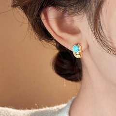 Gold hoop earrings with turquoise oval stone, worn on ear