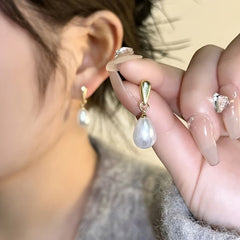 Gold pearl drop earrings with white teardrop pearls, close-up on ear