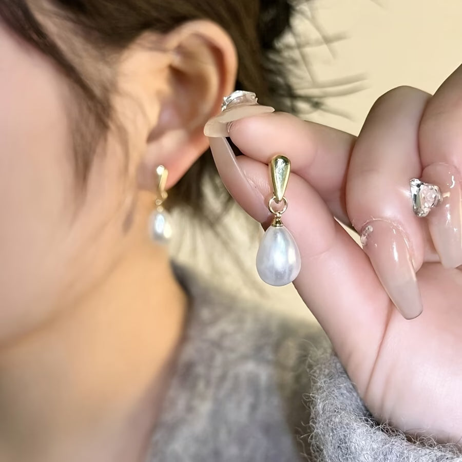 Gold pearl drop earrings with white teardrop pearls, close-up on ear