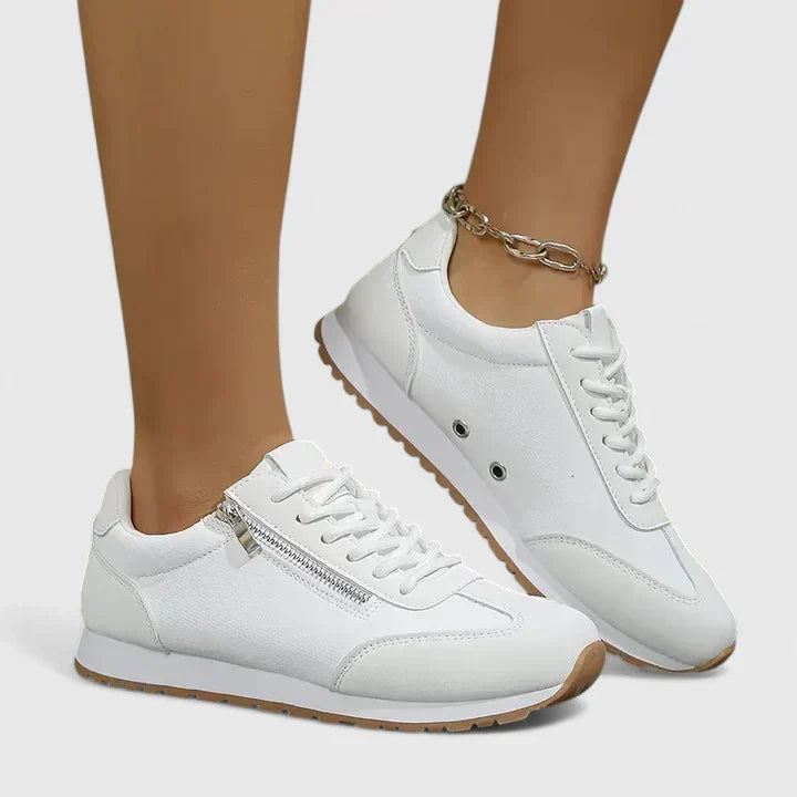 White comfort sneakers with lace-up front, side eyelets, and tan-brown rubber sole