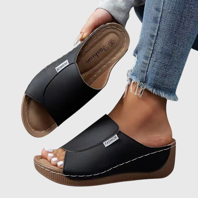Black wedge sandals with wide strap and open toe, stitched trim and textured sole