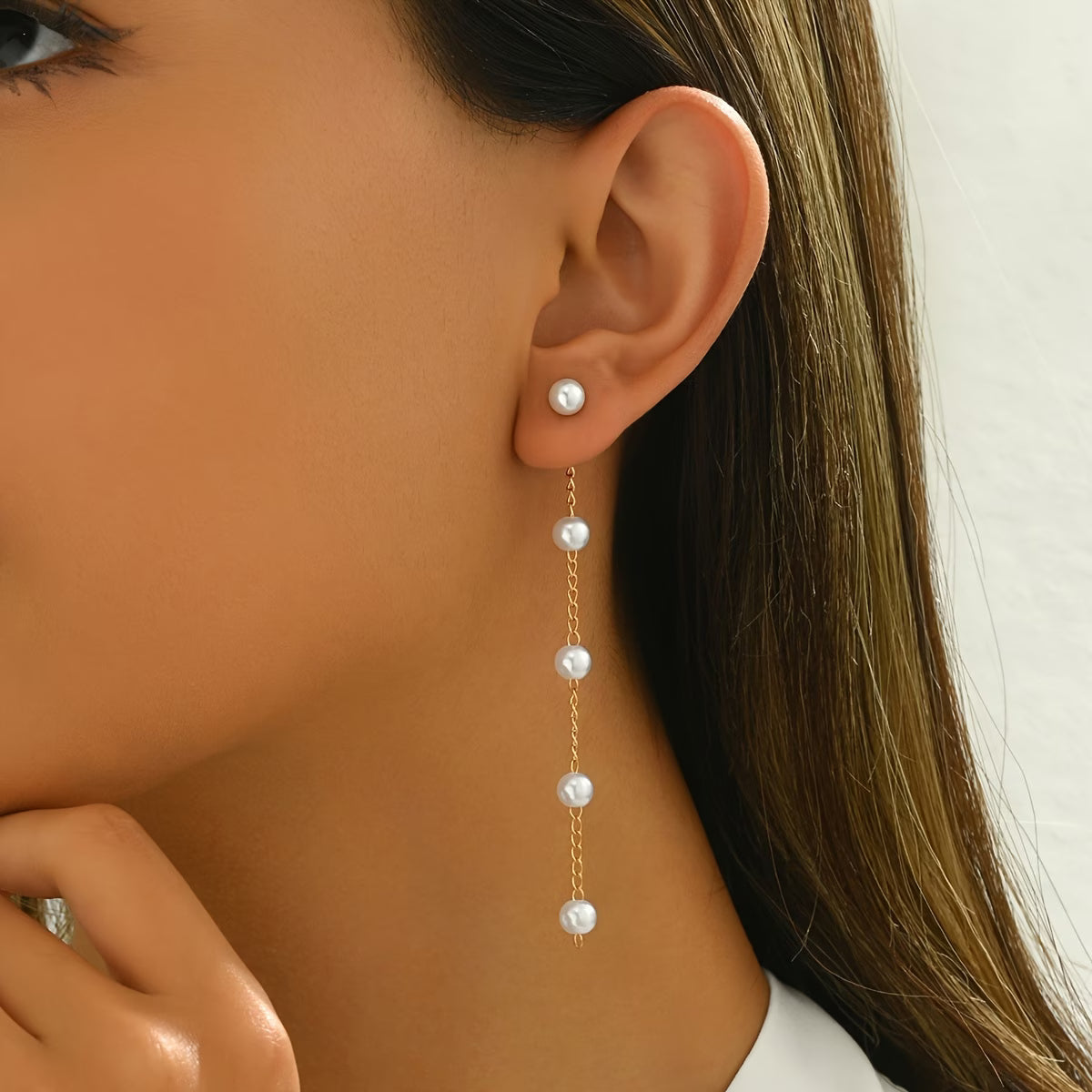 Gold-tone pearl dangle earring with three round white pearl drops on a chain.