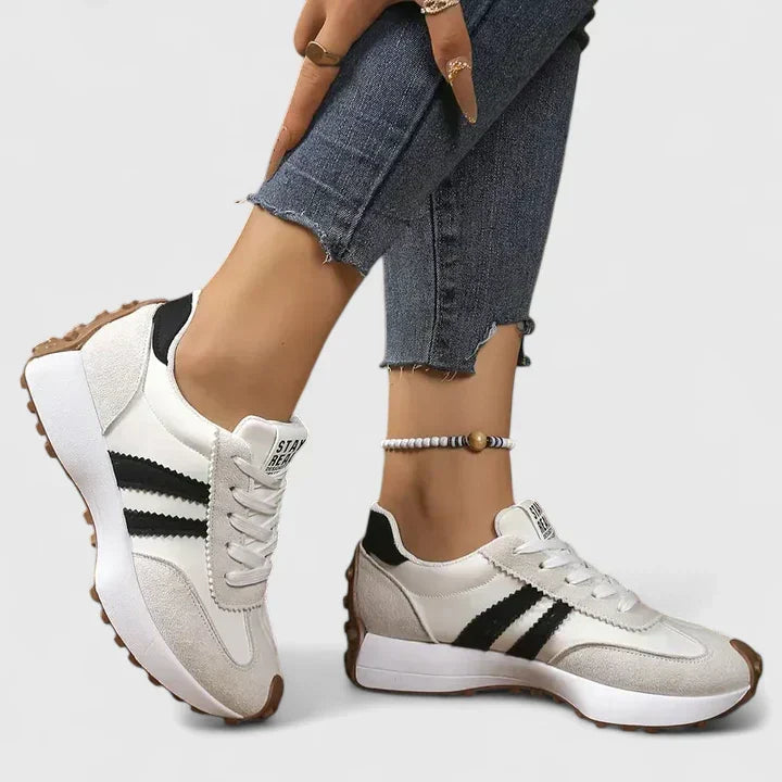 White comfort sneakers with black side stripes and lace-up front, chunky sole