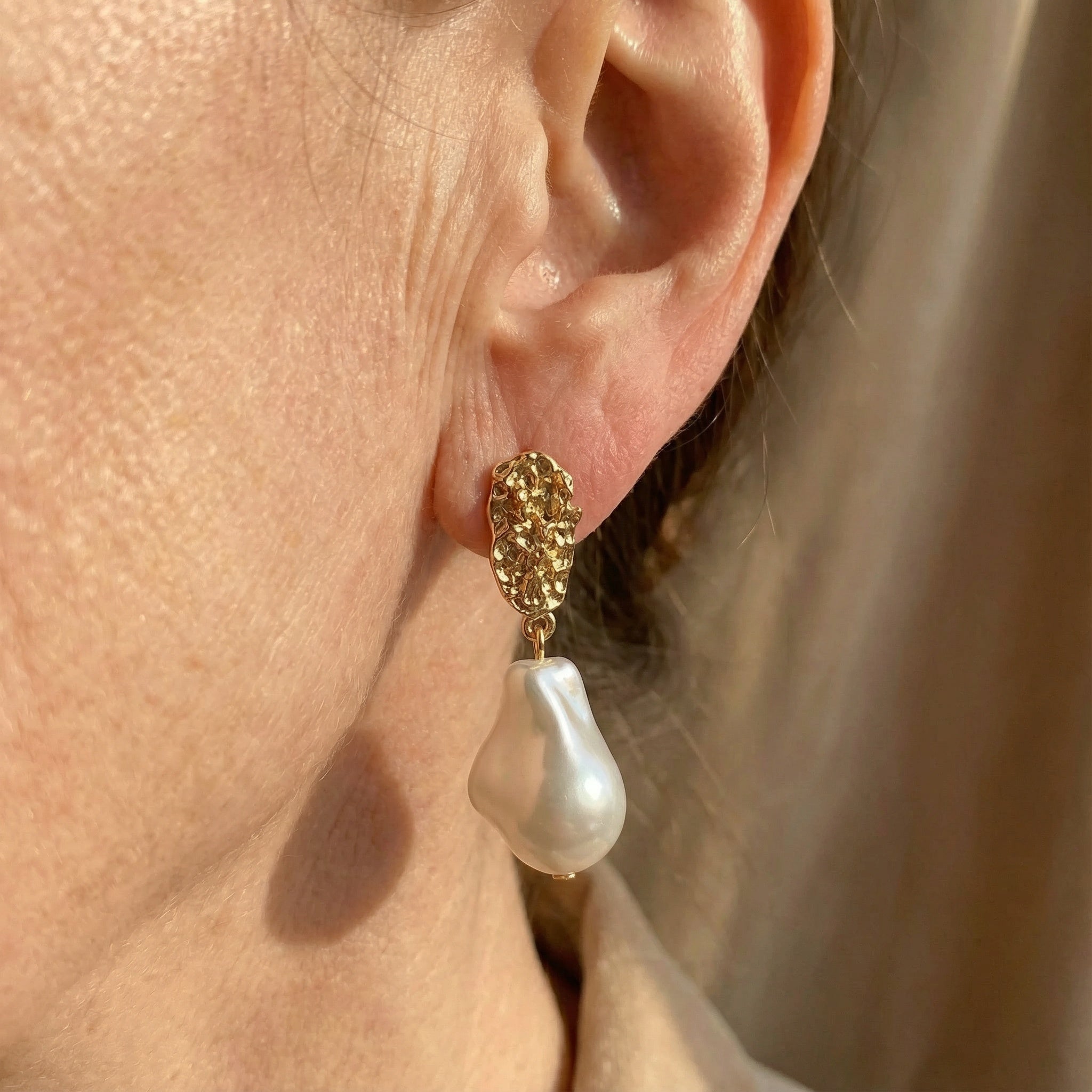 Gold textured hoop earrings with a single white pearl drop on ear