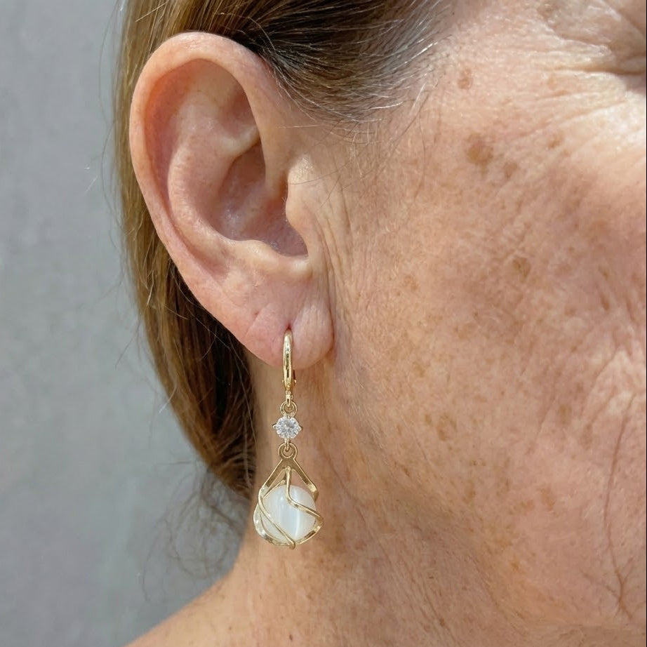 Gold opal drop earrings on ear, teardrop opal and crystal stud details