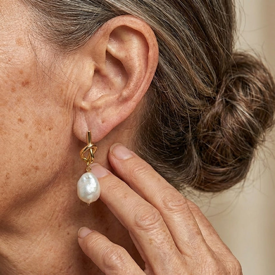 Gold hoop earrings with knotted links and white teardrop pearl drops on ear