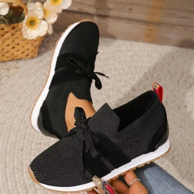 Black comfort sneakers with knit upper, bow laces, and white rubber sole.